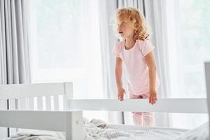 de pie en la cama. una niña linda con ropa informal está en el interior de su casa durante el día foto