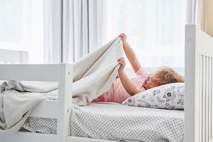 Lying down on the bed. Cute little girl in casual clothes is indoors at home at daytime photo
