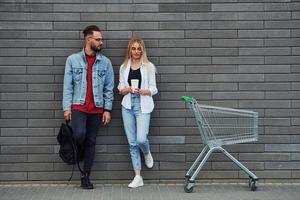 With shopping cart. Young stylish man with woman in casual clothes outdoors together. Conception of friendship or relationships photo