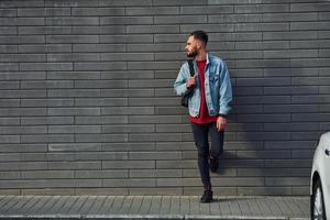 Handsome young guy in casual clothes is outdoors at sunny daytime near white car photo