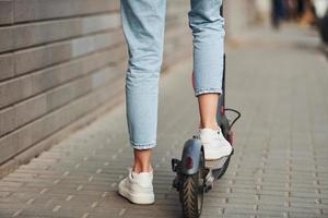 Close up view of girl in casual clothes that riding electric schooter outdoors at sunny daytime photo