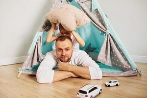 With toy cars. Father and his young young spending time together indoors near tent photo