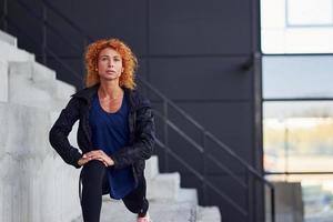 joven pelirroja europea con ropa deportiva haciendo ejercicios en las escaleras al aire libre foto