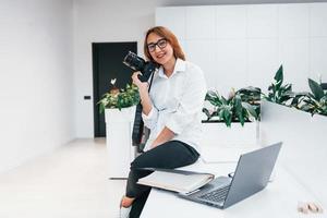 mujer con ropa formal y con cámara sentada en la oficina foto