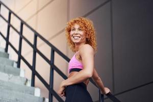 Young european redhead woman in sportive clothes showing her body and posing outdoors after fitness exercises photo