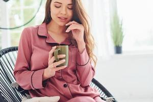 mujer joven alegre en pijama sentada en la silla en el interior durante el día foto