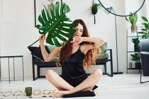 Young woman in pajamas sitting on the floor indoors at daytime and holding big green leaf photo