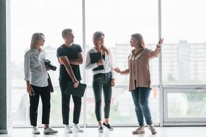 mujer sosteniendo su cámara profesional. grupo de empresarios vestidos de forma formal parados en el interior cerca de una gran ventana foto