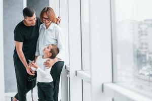 mujer con ropa formal y con cámara en la mano parada dentro de una habitación vacía con un hombre y un niño pequeño foto