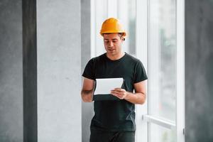 Male worker or engineer in yellow hard hat standing indoors with notepad photo