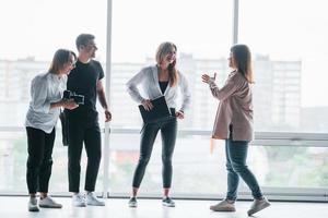 mujer sosteniendo su cámara profesional. grupo de empresarios vestidos de forma formal parados en el interior cerca de una gran ventana foto