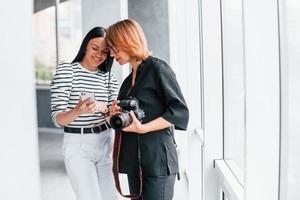 dos mujeres de pie en el interior con cámara y teléfono en las manos foto