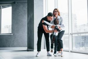 Woman in formal clothes and with camera in hand standing inside of empty room with man and little boy photo