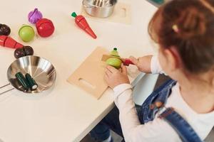 Little girl in casual clothes sits by table and having fun by playing with toys on the kitchen photo