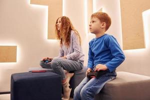 Cheerful kids sitting indoors and playing video games together photo