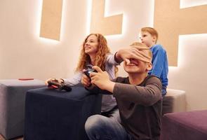 Cheerful kids sitting indoors and playing video games together photo