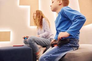 Cheerful kids sitting indoors and playing video games together photo