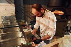 Chef in white clothes preparing delicious pizza on the kitchen of restaurant photo