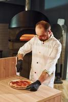 Chef in white clothes preparing delicious pizza on the kitchen of restaurant photo