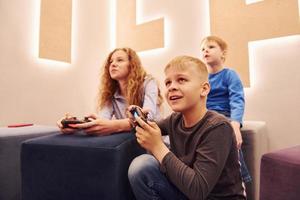 Cheerful kids sitting indoors and playing video games together photo