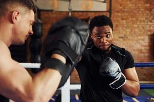 tener el boxeo practicando. un hombre afroamericano con un hombre blanco tiene un día de entrenamiento en el gimnasio foto