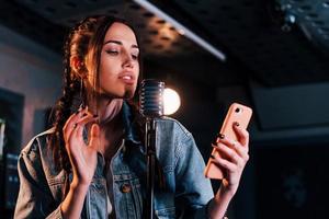 Holding smartphone. Young beautiful female performer rehearsing in a recording studio photo