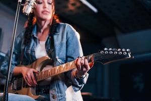 Young beautiful female performer with guitar singing and rehearsing in a recording studio photo