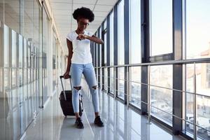 una joven pasajera afroamericana con ropa informal está en el aeropuerto con tiempo de control de equipaje foto