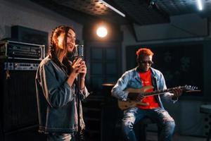 Guy plays guitar, girl sings. African american man with white girl rehearsing in the studio together photo