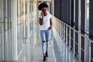 Young african american female passanger in casual clothes is in airport with phone photo