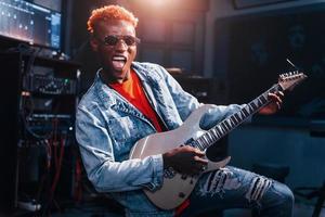 Plays guitar. Young african american performer rehearsing in a recording studio photo