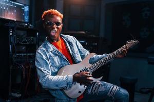 Plays guitar. Young african american performer rehearsing in a recording studio photo