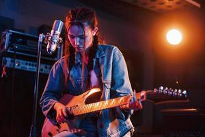 joven y bella intérprete con guitarra cantando y ensayando en un estudio de grabación foto