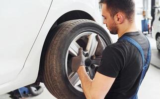 Man in work uniform changing car wheel indoors. Conception of automobile service photo