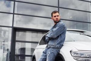 Fashionable man standing near car outdoors against modern business building photo