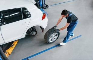 Top view. Man in work uniform walking with car wheel indoors. Conception of automobile service photo