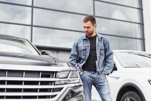 Fashionable man standing near car outdoors against modern business building photo