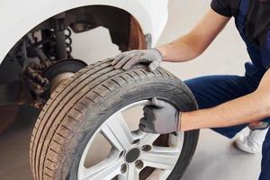 Close up view of man in work uniform with car wheel indoors. Conception of automobile service photo