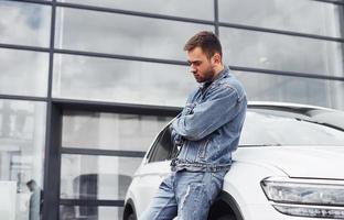 Fashionable man standing near car outdoors against modern business building photo