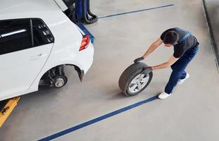 Top view. Man in work uniform walking with car wheel indoors. Conception of automobile service photo