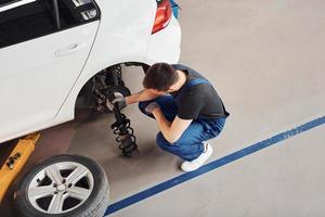 Man in work uniform changing car wheel indoors. Conception of automobile service photo