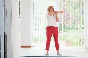 Positive senior woman in sportive clothes indoors at daytime doing exercises photo