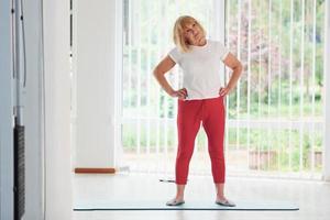 Positive senior woman in sportive clothes indoors at daytime doing exercises photo