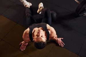 Top view of strong man in sportive clothes that sitting on the floor and takes a break in the gym photo