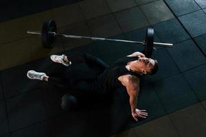 Top view of strong man in sportive clothes that sitting on the floor and takes a break in the gym photo
