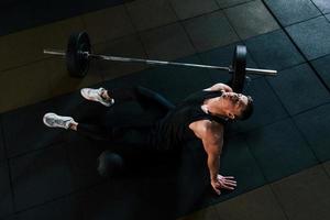 vista superior de un hombre fuerte con ropa deportiva que se sienta en el suelo y toma un descanso en el gimnasio foto