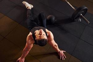 Top view of strong man in sportive clothes that sitting on the floor and takes a break in the gym photo