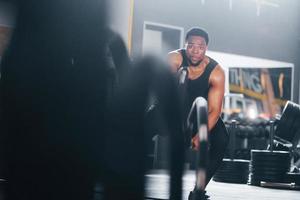 Strong african american man in sportive clothes have workout day in the gym. Doing crossfit by using ropes photo