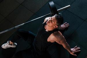 vista superior de un hombre fuerte con ropa deportiva que se sienta en el suelo y toma un descanso en el gimnasio foto