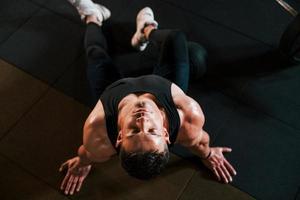 Top view of strong man in sportive clothes that sitting on the floor and takes a break in the gym photo